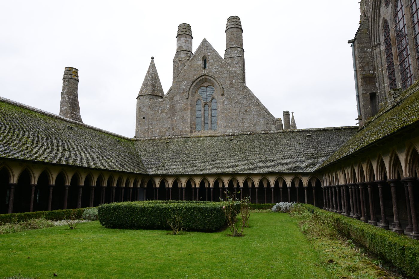 A green courtyard enclosed by the stone arcades of Mont-Saint-Michel’s cloister.