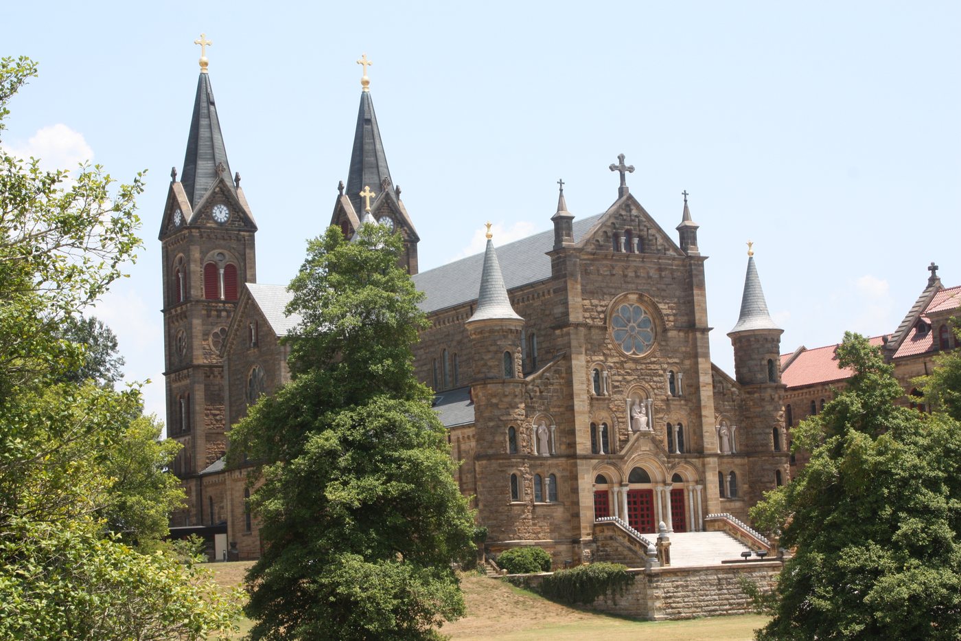 The twin spires and stone facade of Saint Meinrad Archabbey among green trees.